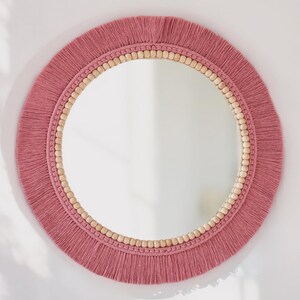 May include: A round mirror with a pink fringe border and a wooden bead trim.