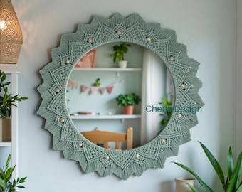 May include: A round wall mirror featuring a sage green macrame frame with a sunburst design, accented by small wooden beads. The mirror displays the text Cherie Design in teal lettering. The intricate knotted cord pattern creates a star-like border.