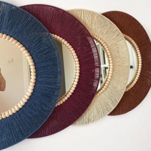 May include: Four circular wall mirrors arranged in a row, each featuring a frame wrapped in colored thread. The frames are navy blue, deep burgundy, beige, and brown, with a border of small, light-colored wooden beads lining the inner edge.