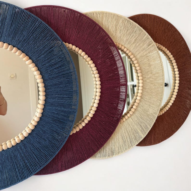 May include: Four circular wall mirrors arranged in a row, each featuring a frame wrapped in colored thread. The frames are navy blue, deep burgundy, beige, and brown, with a border of small, light-colored wooden beads lining the inner edge.
