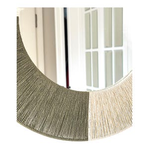 Pode incluir: Um espelho circular com uma moldura envolta em corda enrolada firmemente. A moldura &eacute; dividida em duas se&ccedil;&otilde;es de cores distintas, com um lado em verde-oliva suave e o outro lado em cor creme clara, criando um efeito de dois tons.
