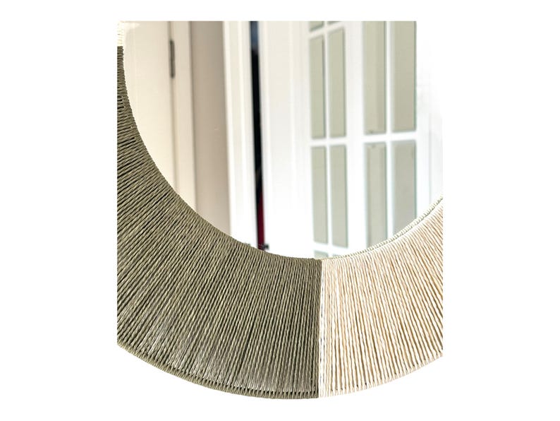 Pode incluir: Um espelho circular com uma moldura envolta em corda enrolada firmemente. A moldura &eacute; dividida em duas se&ccedil;&otilde;es de cores distintas, com um lado em verde-oliva suave e o outro lado em cor creme clara, criando um efeito de dois tons.