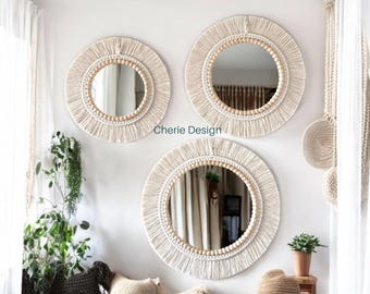 May include: Three round wall mirrors featuring cream-colored macrame fringe borders and natural wooden bead accents. Each mirror is framed by intricate knotted cord patterns. The text Cherie Design is visible between the mirrors.