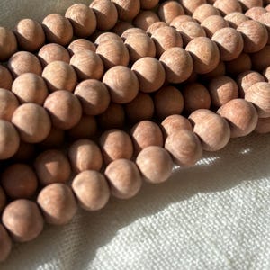 May include: A close-up of a strand of light brown wooden beads. The beads are smooth and round, and they are arranged in a row.