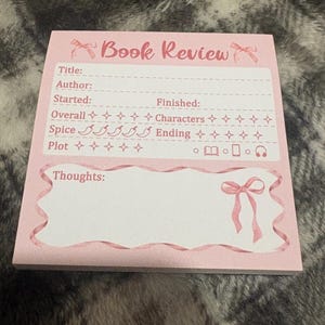 May include: A pink book review notepad with the words "Book Review" at the top. The notepad has sections for title, author, and ratings for overall, spice, and plot. Decorative pink bows are on the top and bottom.