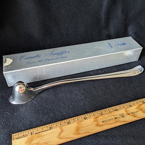 May include: Silver candle snuffer with a long handle and a bell-shaped top. The snuffer is in its original box, which is labeled "Candle Snuffer Circa 1740 Reproduction" and "Gravita".