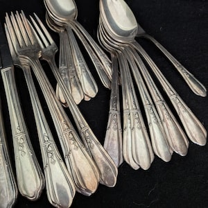 Puede incluir: Una colección de cubiertos de metal plateado que incluye varios tenedores y cucharas dispuestos en grupo. Cada pieza presenta un mango delgado con un patrón de hojas en relieve cerca de la base y un extremo redondeado y liso.
