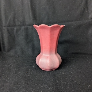 Puede incluir: Un pequeño jarrón de cerámica rosa con un borde festoneado y un acabado texturizado degradado. El jarrón tiene una base redondeada y un cuello acampanado.