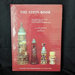 May include: A red book titled "THE STEIN BOOK" with illustrations of beer steins. The book includes information on illustrated catalogs, current prices, and collector's information. The book is by Gary Kirsner & Jim Gruhl and features The Stroh Brewery Co. Collection.