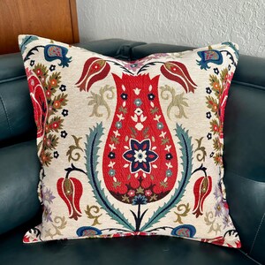 Puede incluir: Una almohada decorativa con un patr&oacute;n floral con tulipanes rojos, azules y verdes sobre un fondo crema.