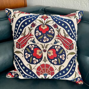 Puede incluir: Una almohada decorativa con fondo blanco y un estampado floral colorido en tonos rojos, azules y verdes. El estampado presenta flores y hojas estilizadas, creando un dise&ntilde;o tradicional y elegante.