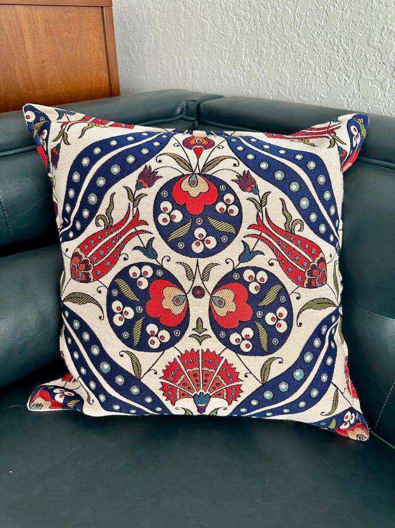 Puede incluir: Una almohada decorativa con fondo blanco y un estampado floral colorido en tonos rojos, azules y verdes. El estampado presenta flores y hojas estilizadas, creando un dise&ntilde;o tradicional y elegante.