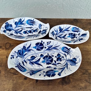 May include: Three blue and white ceramic serving dishes with floral designs. The dishes are oval shaped and have a slight curve on the sides.
