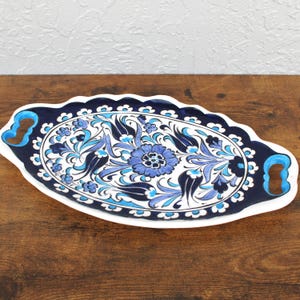 Handpainted oval ceramic tray with blue floral motif and scalloped edges, photographed on wood surface.