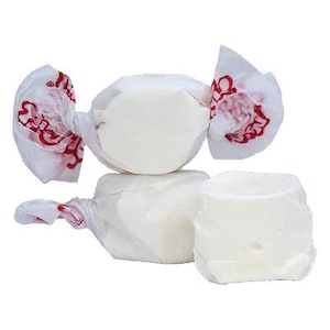 May include: Three white candy pieces wrapped in white paper with red lettering. The candy is in the shape of a cube and a round ball.