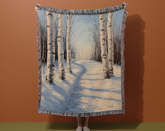 May include: A woven tapestry throw blanket featuring a winter scene of a snowy path winding through a birch tree forest. The trees are white with black markings and the path is covered in snow.