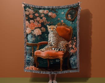 Op de afbeelding: Een geweven tapijtdeken met een cheetah op een rode fauteuil. De achtergrond is een teal bloemenontwerp met roze rozen en antieke vazen. De deken heeft een gefranjerde rand.