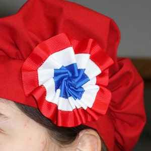 May include: A red fabric hat with a large, white, blue, and red rosette.