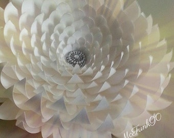 May include: A large white paper flower with a sparkly center. The flower is made of many layers of paper, creating a 3D effect.