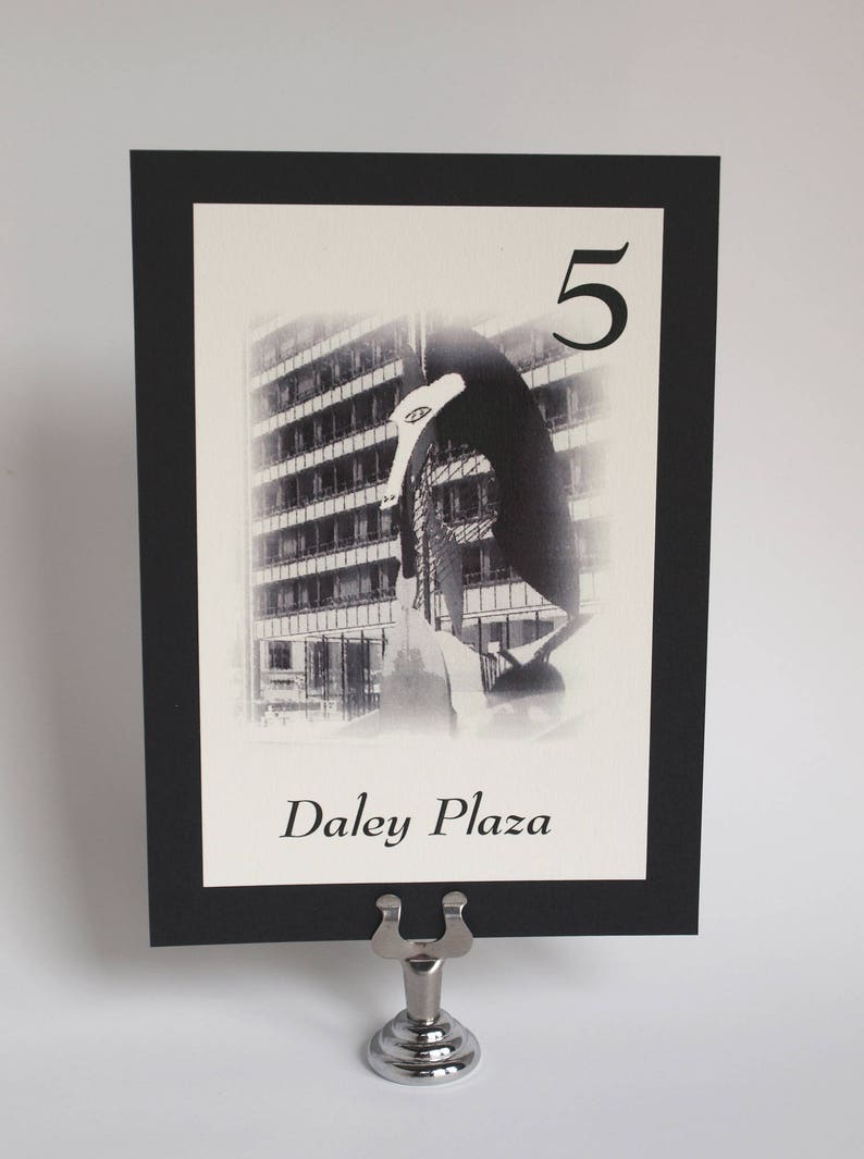May include: Black and white photo of a building with a sculpture in front of it. The photo is on a black card with a white border. The card has the number "5" and the text "Daley Plaza" printed on it.