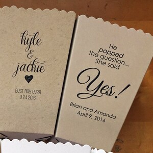 Pode incluir: Duas caixas de pipoca de papel castanho com texto. A primeira caixa diz "kyle & jackie" com um cora&ccedil;&atilde;o e "BEST DAY EVER 9.24.2016". A segunda caixa diz "He popped the question... She said Yes!" com "Brian and Amanda April 9, 2016" abaixo.