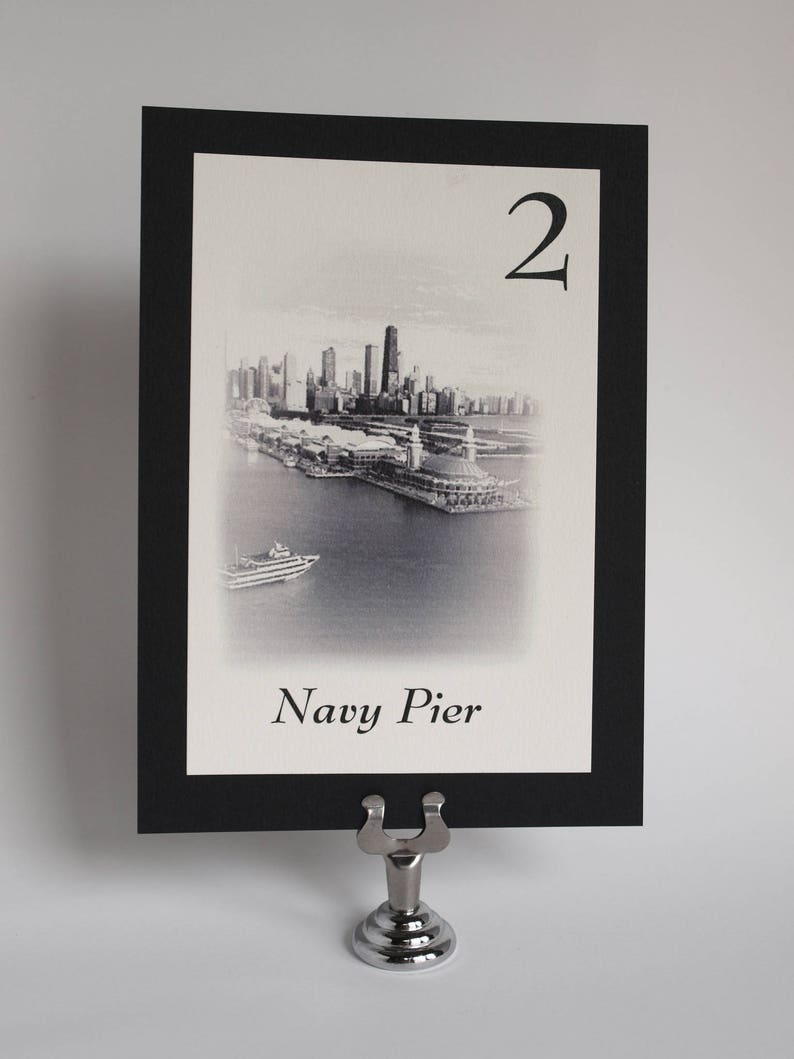 May include: Black and white photo of the Chicago skyline with the text "Navy Pier" and the number "2" on a white card with a black border. The card is in a silver table number holder.