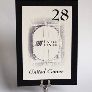May include: Black and white table number card with a photo of the United Center in Chicago. The number 28 is printed in black at the top of the card. The text "United Center" is printed in black at the bottom of the card.