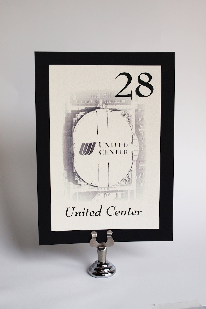 May include: Black and white table number card with a photo of the United Center in Chicago. The number 28 is printed in black at the top of the card. The text "United Center" is printed in black at the bottom of the card.