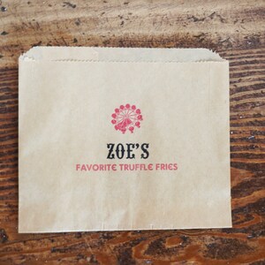 Op de afbeelding: Een bruine papieren zak met een rood en zwart logo met de tekst "ZOE'S FAVORITE TRUFFLE FRIES".