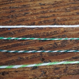 Pu&ograve; includere: Quattro pezzi di spago su una superficie di legno. Lo spago &egrave; bianco, verde e bianco, verde e bianco e verde chiaro e bianco.