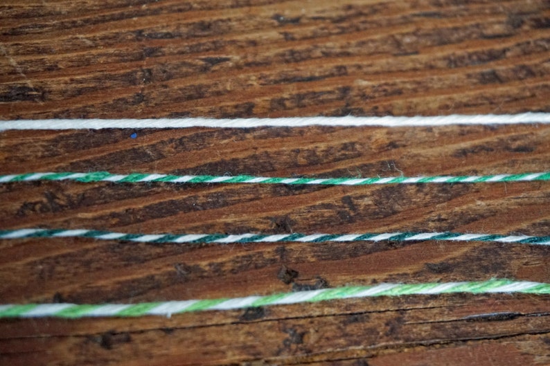 Pu&ograve; includere: Quattro pezzi di spago su una superficie di legno. Lo spago &egrave; bianco, verde e bianco, verde e bianco e verde chiaro e bianco.
