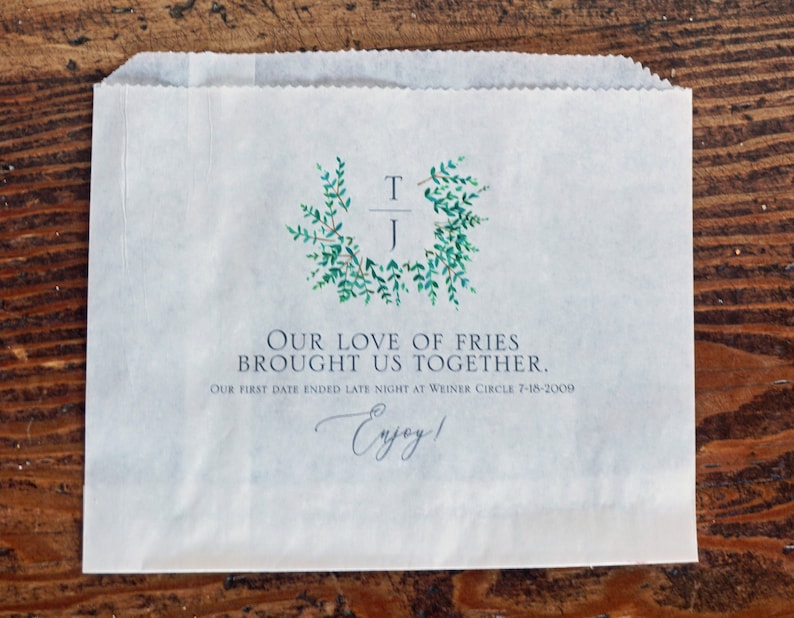 Op de afbeelding: Een witte papieren zak met een groen bladerontwerp en de tekst "Our love of fries brought us together. Our first date ended late night at Weiner Circle 7-18-2009. Enjoy!"
