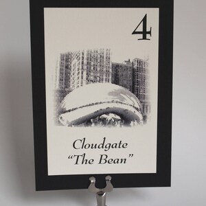 May include: Black and white table number card with a black border. The card features a photo of Cloudgate, also known as "The Bean", a public sculpture in Chicago. The number "4" is printed in the top right corner of the card.