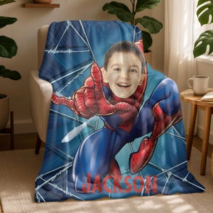 Puede incluir: Una manta azul con una imagen personalizada de la cara de un ni&ntilde;o superpuesta a una ilustraci&oacute;n de Spider-Man. La manta tiene un fondo azul con un dise&ntilde;o de telara&ntilde;a y el nombre "JACKSON" en rojo.