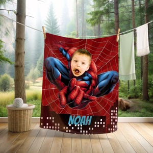 Puede incluir: Una toalla roja y azul con tem&aacute;tica de Spider-Man con la cara de un ni&ntilde;o superpuesta en el cuerpo del superh&eacute;roe. La toalla tiene un dise&ntilde;o de telara&ntilde;a roja y el nombre "NOAH" en letras blancas. La toalla est&aacute; colgada en un tendedero.