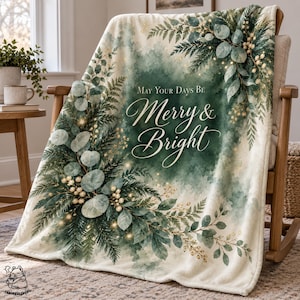 May include: A soft throw blanket featuring a watercolor-style design of green eucalyptus leaves, pine branches, and white berries. The center displays the text "May Your Days Be Merry & Bright" in elegant white script against a dark green background.