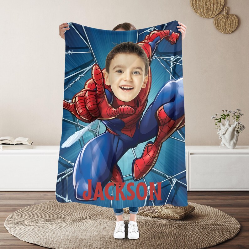 Puede incluir: Una manta azul y roja con tem&aacute;tica de Spider-Man con un recorte de cara personalizado. La manta presenta un gr&aacute;fico de Spider-Man en acci&oacute;n, con el nombre "JACKSON" impreso en rojo. El recorte de la cara es de un ni&ntilde;o.