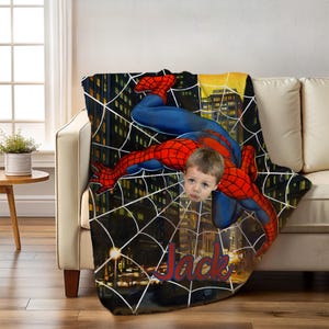 Puede incluir: Una manta personalizada con Spider-Man en una pose din&aacute;mica contra un fondo de paisaje urbano. La manta tiene un nombre personalizado en escritura roja. El dise&ntilde;o incluye la cara de un ni&ntilde;o integrada en la imagen del superh&eacute;roe.