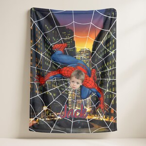 Puede incluir: Una manta personalizada con un dise&ntilde;o de Spiderman con la cara de un ni&ntilde;o superpuesta al personaje. La manta tiene un fondo de paisaje urbano con un dise&ntilde;o de telara&ntilde;a y el nombre "Jack" en escritura roja.