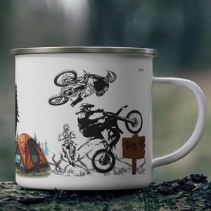 May include: White enamel mug featuring black illustrations of motocross riders performing stunts. The mug also depicts a campsite with a tent and trees, and a sign that says "Day Off". The mug has a silver rim and a white handle.