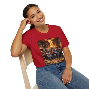 Könnte beinhalten: Ein rotes Crop-Top mit einem Grafikdruck, der einen Raum voller Menschen, Pizza und Feuer zeigt. Das Bild ist auf ein rotes T-Shirt gedruckt. Das Model trägt eine blaue Jeans und Goldschmuck.