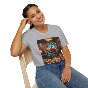 Könnte beinhalten: Hellgraues T-Shirt mit einem farbenfrohen Grafikdesign, das zwei Personen auf einem Sofa zeigt, umgeben von Pizza und Snacks. Die Grafik zeigt eine detaillierte Innenszene mit einer leuchtenden Leuchte und schwebenden Pizzastücken.