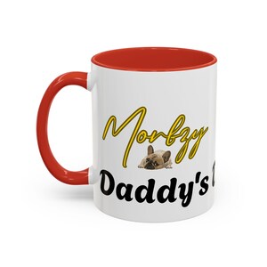 Könnte beinhalten: Weißer Keramikbecher mit rotem Innenraum und Griff. Der Becher zeigt den Text "Morby Daddy's" in einer Mischung aus Schreibschrift und Blockbuchstaben sowie ein Bild einer Französischen Bulldogge.