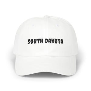 Peut inclure: Casquette de baseball blanche avec l'inscription "SOUTH DAKOTA" en lettres noires stylisées sur le devant. La casquette a une visière incurvée et une couronne arrondie. Un accessoire décontracté.