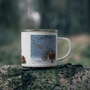May include: White enamel camping mug with a silver rim. The mug features a winter scene with a motorcycle and the text "Day 4". A tent is also visible on the side of the mug. The mug is sitting on a log.