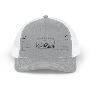 Peut inclure: Casquette de camionneur grise avec un dos en filet blanc. L'avant de la casquette affiche le texte "4 The Mount Rushmore State" et "South Dakota Est 1889" avec un graphique du Mont Rushmore. Le côté droit porte le texte "Under God the People Rule".
