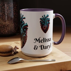 Puede incluir: Taza de cerámica blanca con interior y asa morados. La taza presenta dos diseños de corazón anatómico estilizados en verde azulado y rojo. Los nombres "Melissa & Daryl" están impresos en negro.