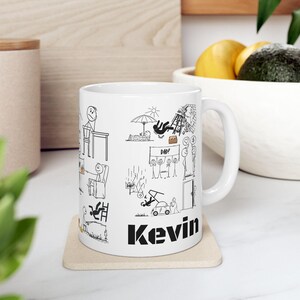 Puede incluir: Taza de cerámica blanca con ilustraciones de figuras de palo negras que representan varios escenarios, incluyendo una persona en un escritorio y una persona cayendo de una escalera. El nombre "Kevin" está impreso en letras negras en negrita.