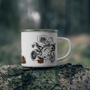 May include: White enamel mug featuring a black and white illustration of a motorcycle and rider with a thought bubble. The mug has a silver rim and handle, with the text "Wing It" on a small sign.