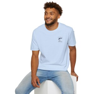 Pode incluir: Uma camiseta azul claro com um pequeno gráfico de um pássaro no peito esquerdo. A camiseta tem gola redonda e mangas curtas.